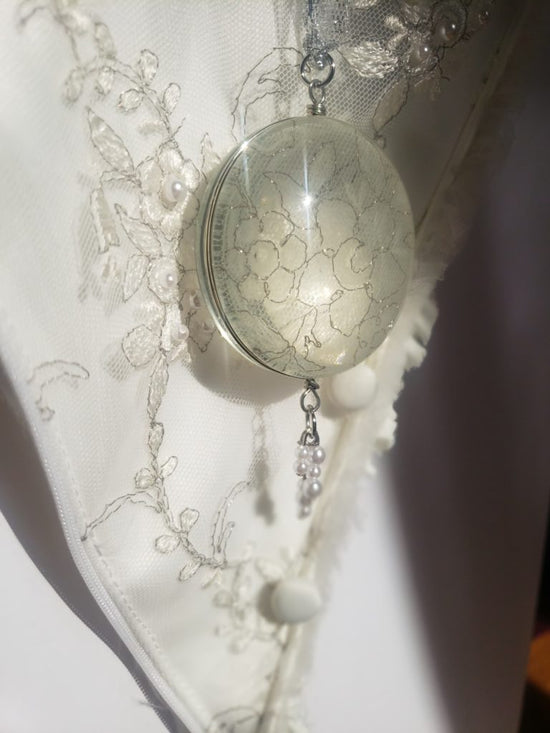 Glass pendant filled with white lace on a white lace background 