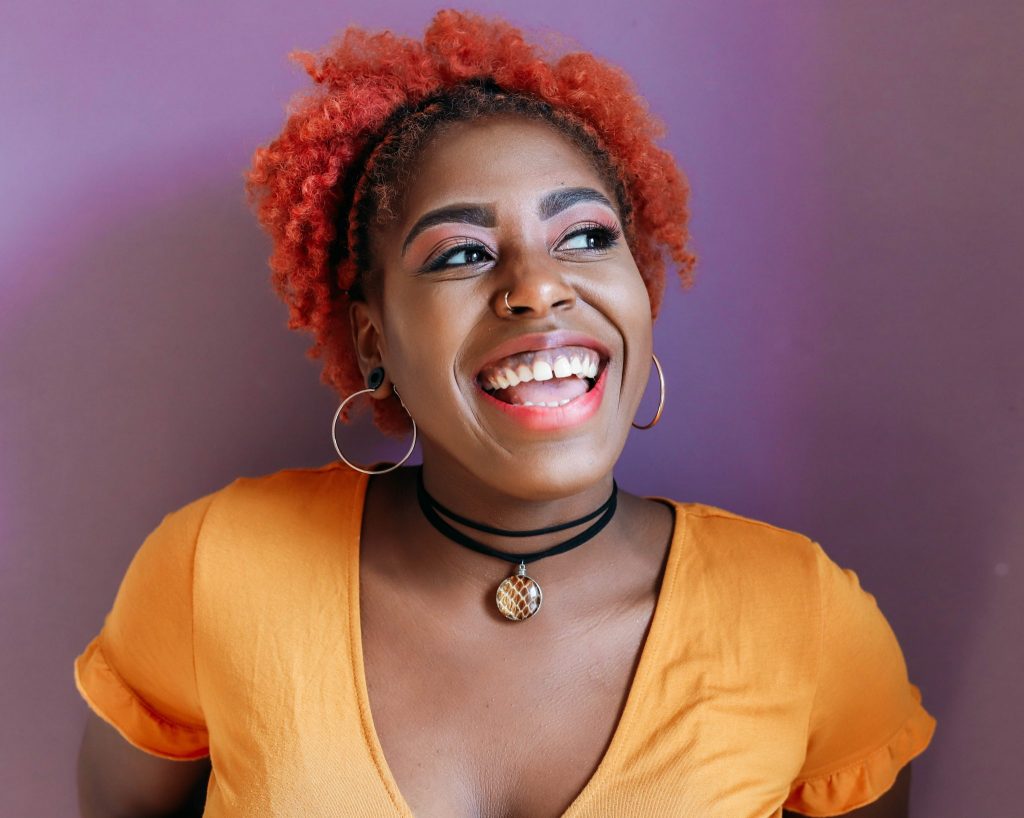 Black girl with red hair and orange shirt wearing Shed Snakeskin & Gold Leaf Pendant on a black cord with a purple background