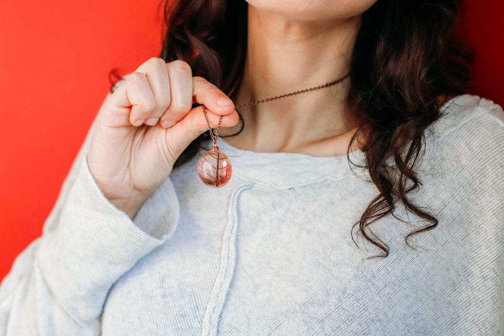 Close up of white girl with brown hair wearing a Pink Leaf Pendant on a copper chair with a red background