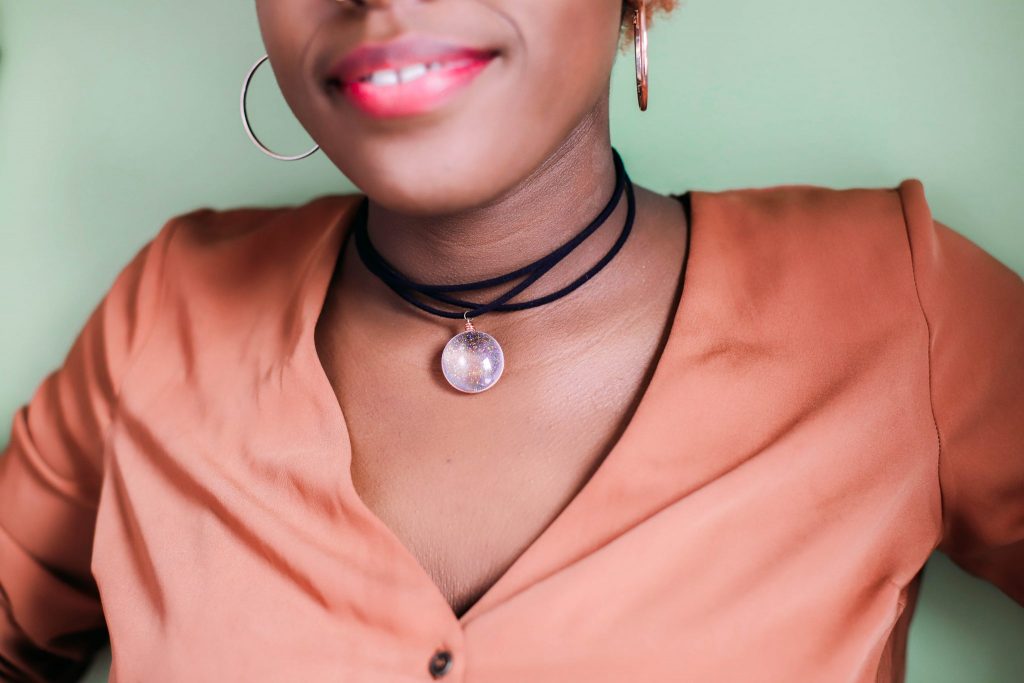 Close up of black girl wearing a glitter pendant on a black cord with a light green background