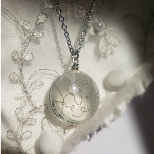 glass pendant filled with white lace on a silver chain on a white lace background 