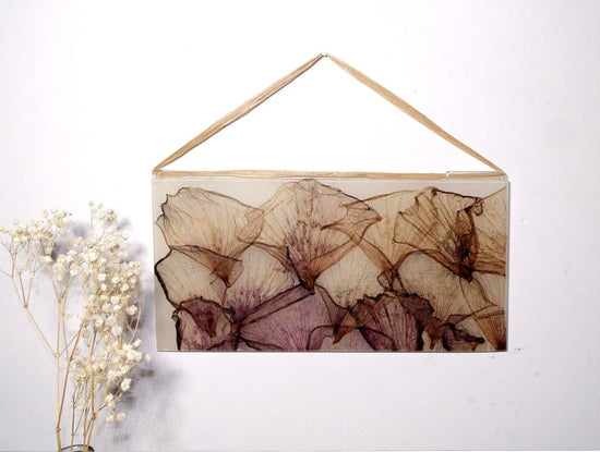 Rectangular glass wall hanging containing brown flowers on a white wall