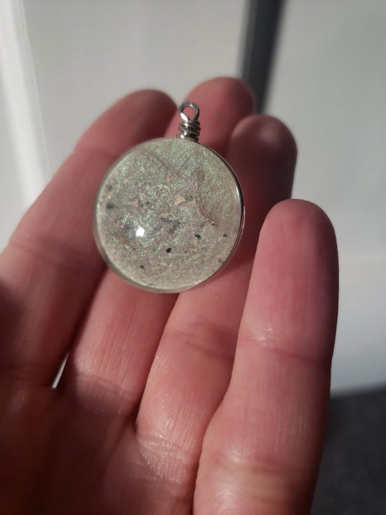White hand holding glass pendant with glitter inside 