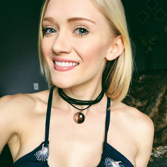 White girl with blond hair wearing a black leather wrap choker with a glass pendant wearing a sleeveless top