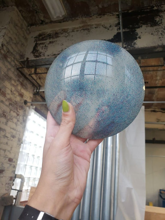 White hand holding up large glass orb containing blue glitter