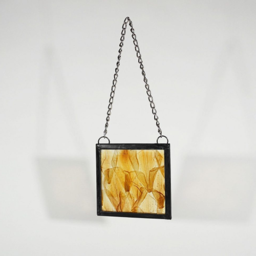 Square glass wall hanging containing yellow flower petals on a white background