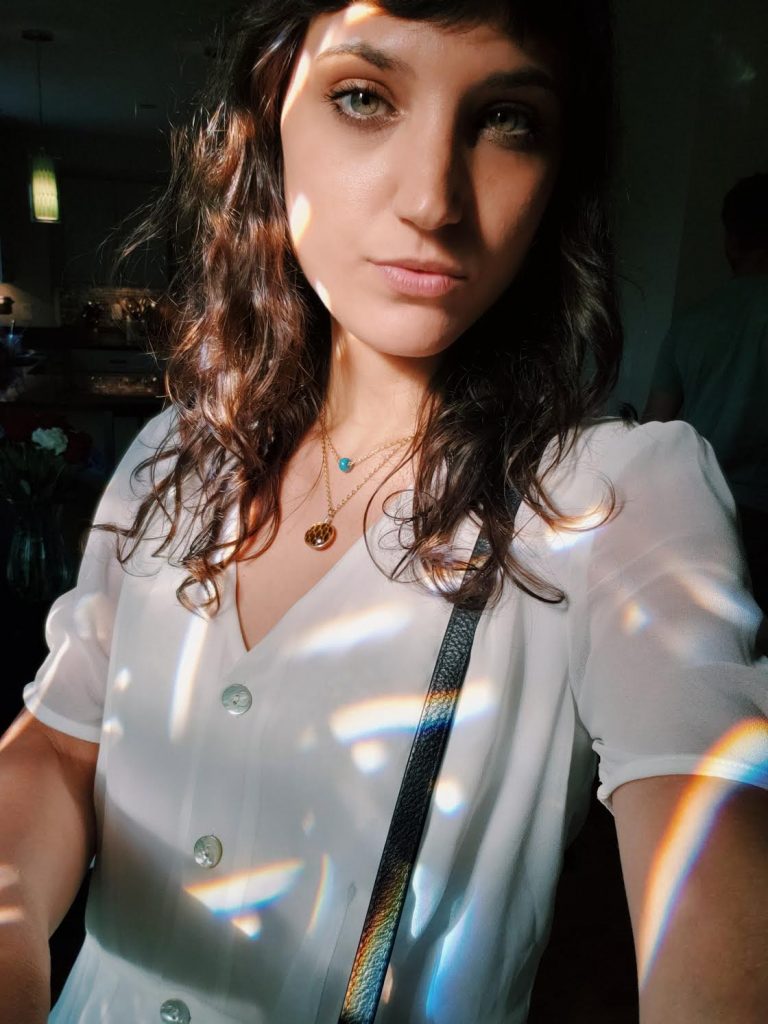 White girl with brown hair and white shirt wearing a Mini Shed Snakeskin Vision Pendant and covered in Rainbow Prisms