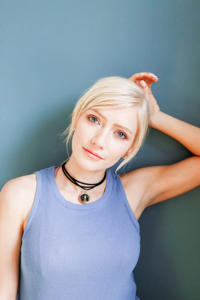 White girl with blond hair and blue shirt wearing a gilded Pheasant Feather pendant on a black leather cord wrapped three times on a blue background