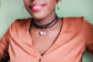 Close up of black girl wearing a glitter pendant on a black cord with a light green background