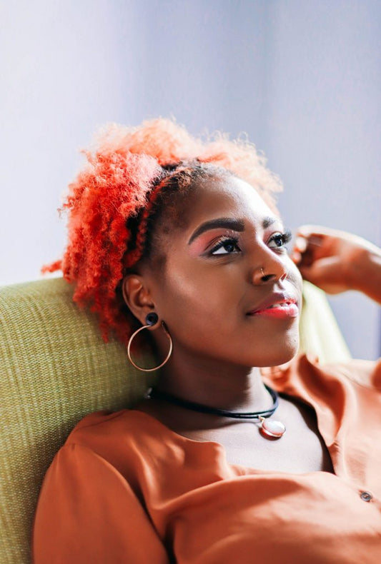 Black girl with red hair sitting on green couch wearing a Pearlescent Pendant on a black cord