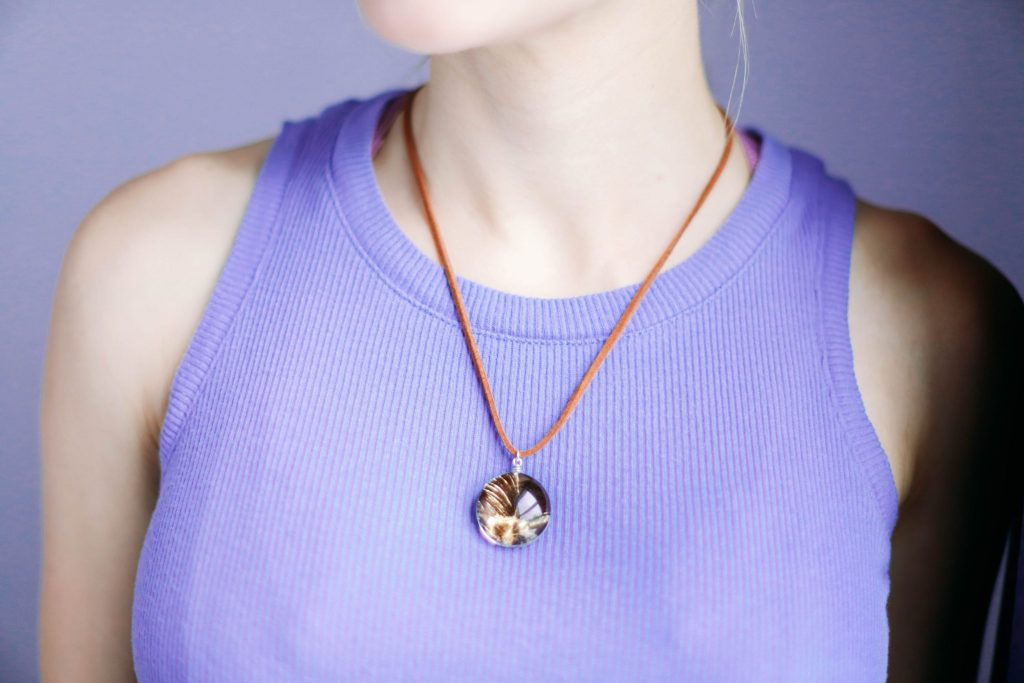 Close up of white girl wearing the gilded pheasant feather necklace on a brown leather cord. She's wearing a purple tank top