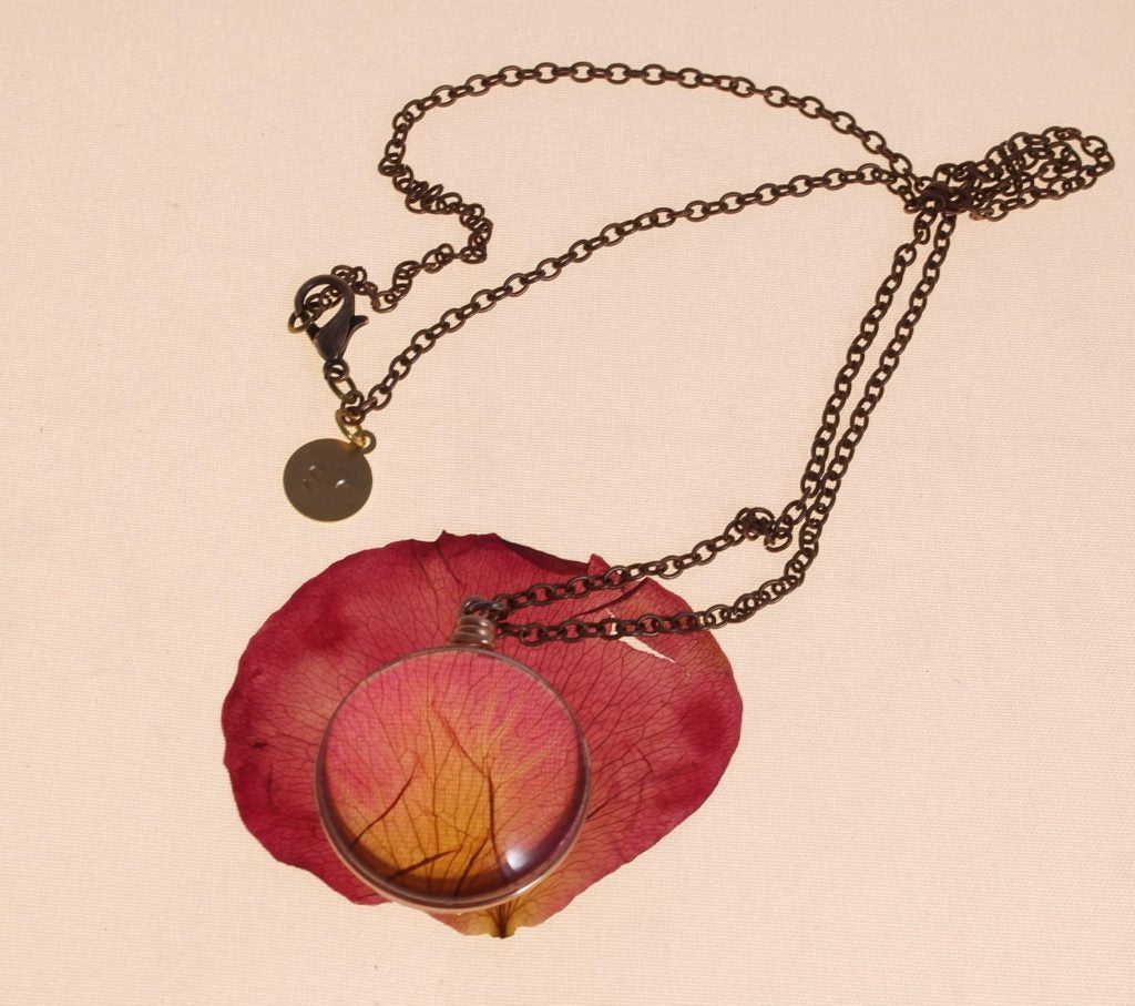 Rose Petal Pendant on a copper chain laying on its original rose petal on a white background