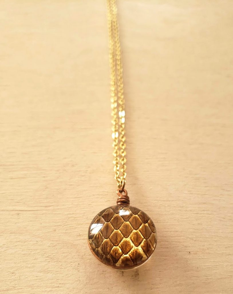 Mini Shed Snakeskin Vision Pendant on a gold chain laying on a wooden background